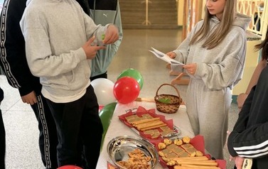 Na zdjęciu widzimy uczni&oacute;w na holu szkolnym podczas przerwy. Uczniowie biorą udział w quizie wiedzy na temat Włoch. Dookoła znajduje się dekoracja w kolorach włoskich, uczniowie biorą r&oacute;wnież udział w poczęstunku włoskim.