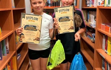 Trzy uczennice pozują do zdjęcia z dyplomami w bibliotece szkolnej