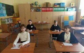 Na zdjęciu widzimy dzieci  sali lekcyjnej siedzących przy ławkach czekających na rozpoczęcie konkursu, przed nimi na ławkach leżą testy.