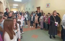 Na zdjęciu widzimy osoby dorosłe i dzieci czekające na rozpoczęcie konkursu. Wszyscy znajdują się na korytarzu szkolnym.