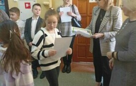 Na zdjęciu widzimy p. dyrektor MZEiA i dyrektor szkoły , Panie wręczają dyplom uczennicy. W tle inne dzieci.