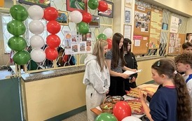 Na zdjęciu widzimy uczni&oacute;w na holu szkolnym podczas przerwy. Uczniowie biorą udział w quizie wiedzy na temat Włoch. Dookoła znajduje się dekoracja w kolorach włoskich, uczniowie biorą r&oacute;wnież udział w poczęstunku włoskim