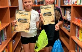 Trzy uczennice pozują do zdjęcia z dyplomami w bibliotece szkolnej