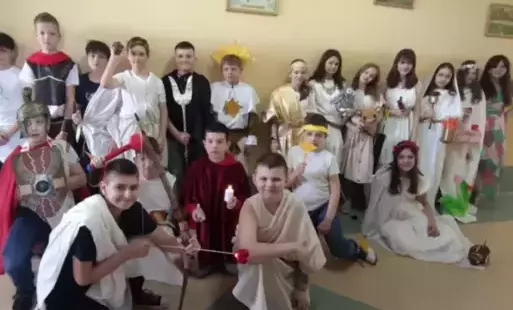 Uczniowie na korytarzu szkolnym pozują do zdjęcia grupowego przebrani za greckich bogów