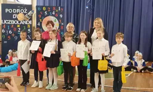 Na zdjęciu widzimy grupę dzieci w towarzystwie dyrektor szkoły SP3 i p. Burmistrz na sali gimnastycznej na konkursie matematycznym 