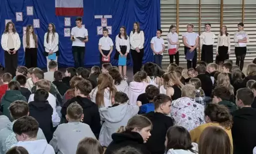 Na zdjęciu widzimy uczniów na sali gimnastycznej ubranych w odświętne stroje podczas apelu z okazji 3-go Maja