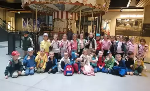 Grupa uczniów z klasy Zero, pozuje do zdjęcia za nimi w tle kolorowa karuzela