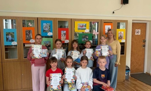 Na zdjęciu widzimy grupę uczniów z klas młodszych z nagrodami i dyplomami w ręku. Uczniowie znajdują się w bibliotece szkolnej za nimi w tle prezentujące się prace konkursowe.