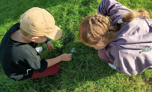 Na zdjęciu dwie uczennice oglądające roślinkę przez lupę