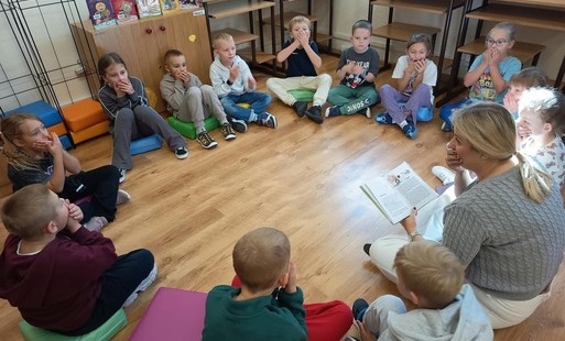 Uczniowie siedzą w kręgu i słuchają głośnego czytania.